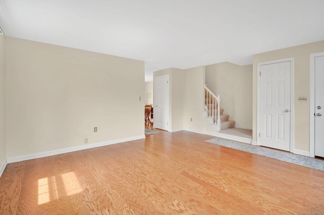 unfurnished living room featuring baseboards, stairway, and light wood-style floors