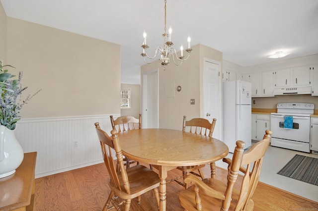 dining space with a wainscoted wall, light wood finished floors, and a notable chandelier