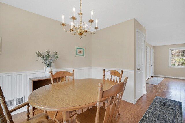 dining area with a notable chandelier, wood finished floors, visible vents, and a wainscoted wall