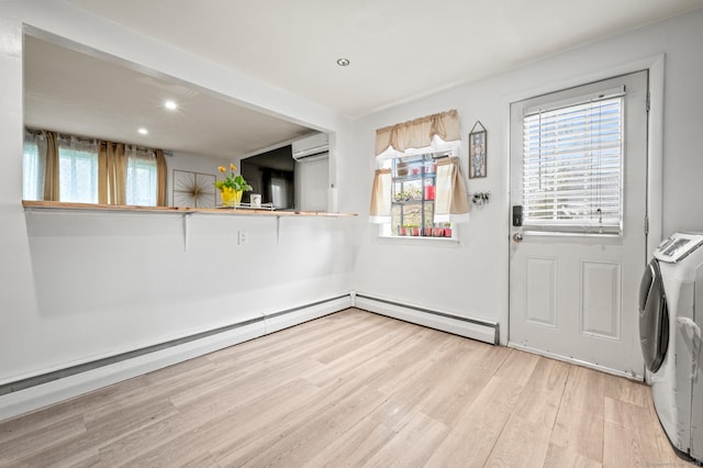 interior space with light wood-style floors, a baseboard heating unit, a wall mounted air conditioner, and a healthy amount of sunlight