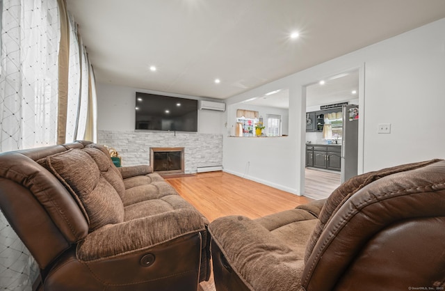living room featuring an AC wall unit, a stone fireplace, recessed lighting, wood finished floors, and a baseboard radiator