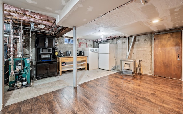 finished basement featuring freestanding refrigerator, a heating unit, wood finished floors, and a wood stove