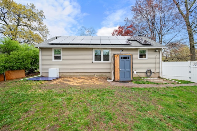 back of property featuring roof mounted solar panels, fence, and a yard