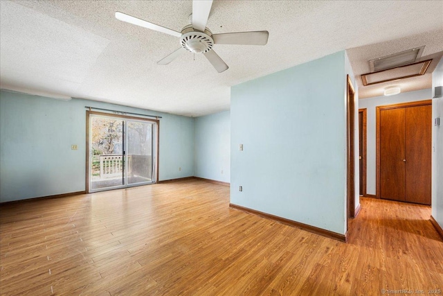 spare room featuring wood finished floors, attic access, ceiling fan, baseboards, and a textured ceiling