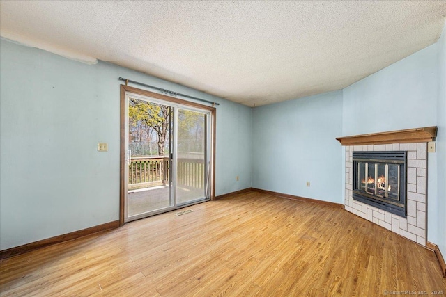 unfurnished living room featuring light wood finished floors, a textured ceiling, a tiled fireplace, and baseboards