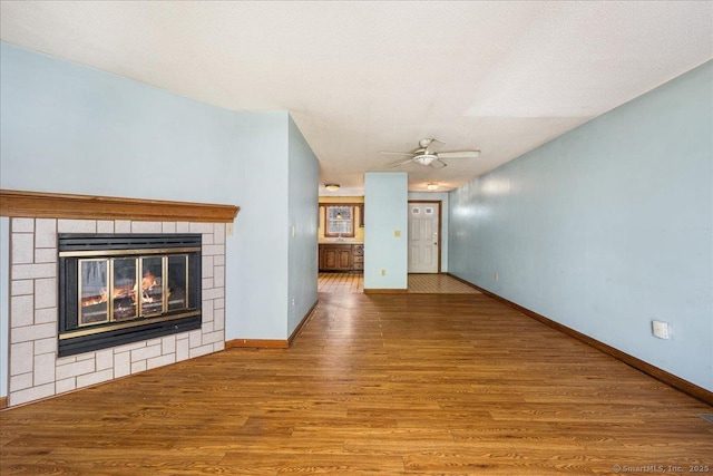 unfurnished living room featuring a glass covered fireplace, wood finished floors, a ceiling fan, and baseboards