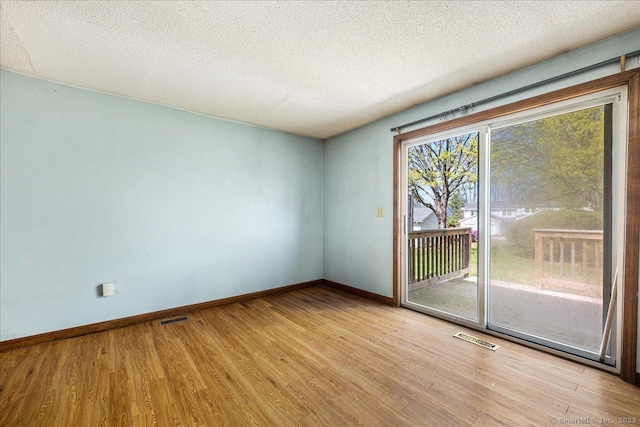 unfurnished room with wood finished floors, visible vents, a textured ceiling, and baseboards