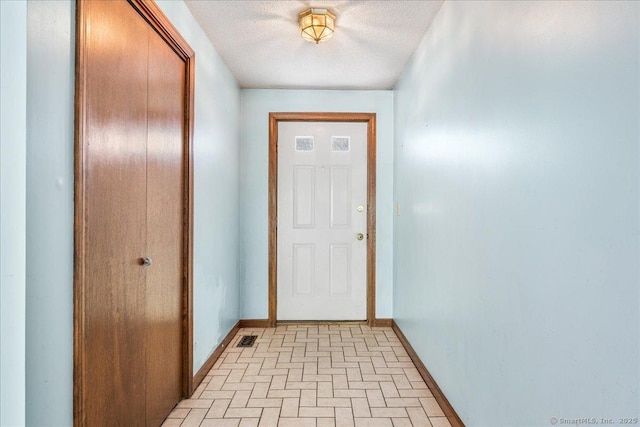 doorway featuring a textured ceiling, visible vents, brick patterned floor, and baseboards