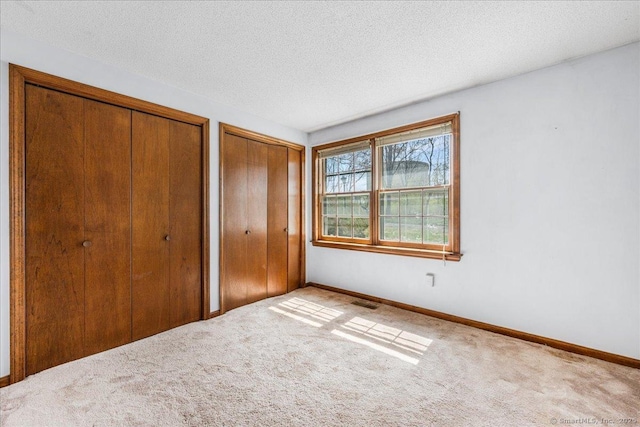 unfurnished bedroom with visible vents, multiple closets, baseboards, and carpet floors