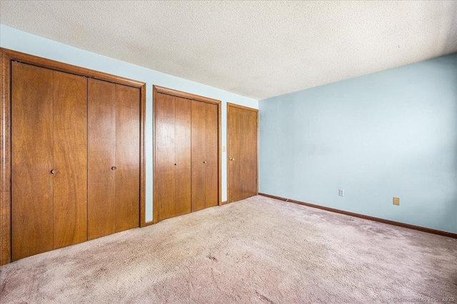 unfurnished bedroom with two closets, a textured ceiling, and carpet