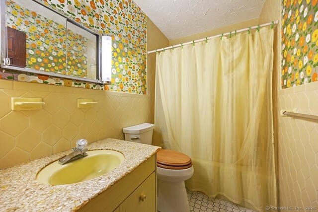 bathroom with wallpapered walls, a wainscoted wall, toilet, vanity, and a shower with curtain