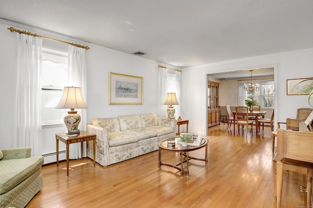living area featuring visible vents, a notable chandelier, light wood-style flooring, and a baseboard radiator