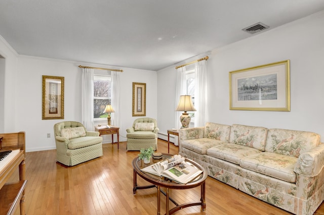 living area featuring baseboard heating, wood-type flooring, baseboards, visible vents, and crown molding