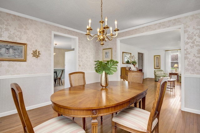 dining room with an inviting chandelier, wallpapered walls, ornamental molding, a wainscoted wall, and wood-type flooring