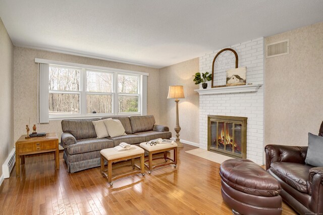 living area with a brick fireplace, visible vents, hardwood / wood-style floors, wallpapered walls, and a baseboard radiator