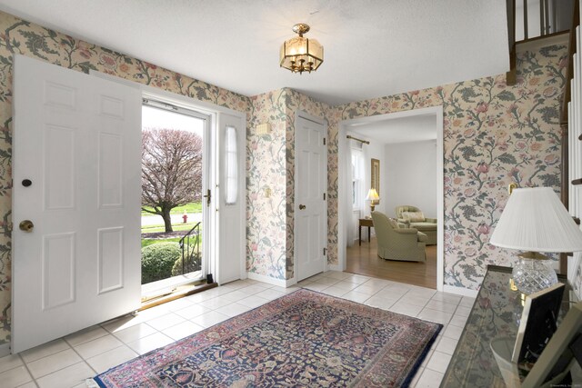 foyer entrance with light tile patterned flooring, wallpapered walls, and baseboards