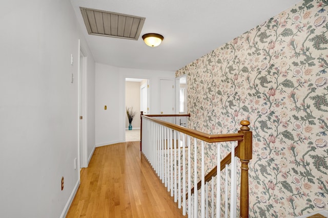hallway featuring wallpapered walls, light wood-style floors, an upstairs landing, baseboards, and visible vents