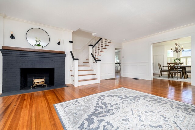 living room featuring stairs, an inviting chandelier, ornamental molding, and wood finished floors