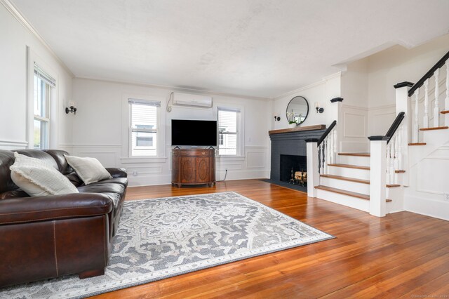 living room featuring a wall mounted AC, wood finished floors, stairway, ornamental molding, and a decorative wall