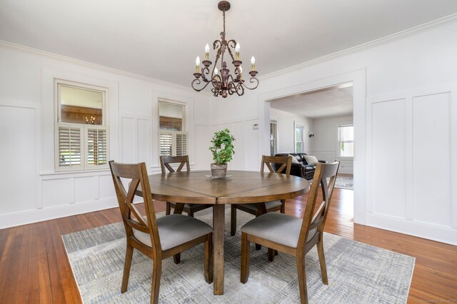 dining room featuring wood finished floors, ornamental molding, a decorative wall, and a notable chandelier