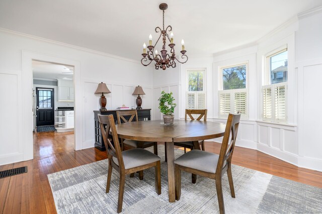 dining area with a notable chandelier, wood-type flooring, a decorative wall, and visible vents