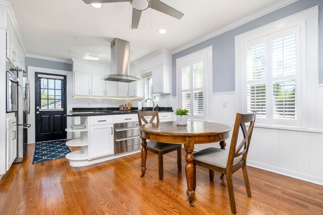 dining space with ceiling fan, ornamental molding, a decorative wall, and light wood-style flooring