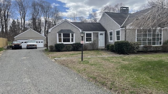 view of front of property featuring a front lawn, a detached garage, a chimney, a shingled roof, and an outdoor structure