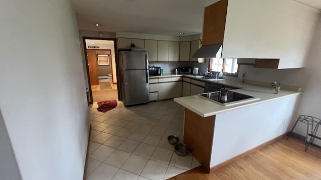 kitchen with light countertops, light tile patterned floors, a sink, black appliances, and a peninsula