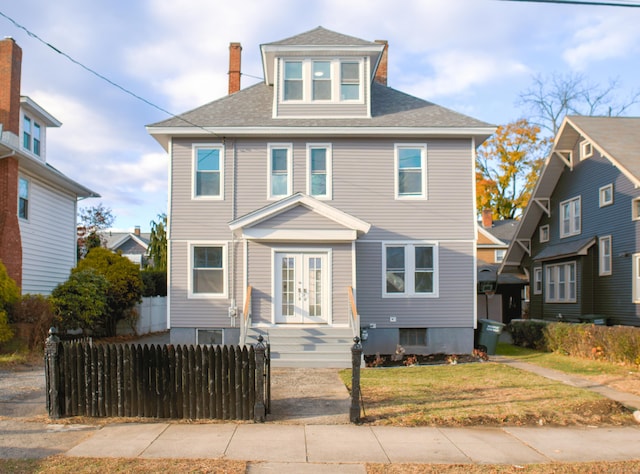 traditional style home featuring french doors, roof with shingles, a front lawn, a fenced front yard, and a chimney