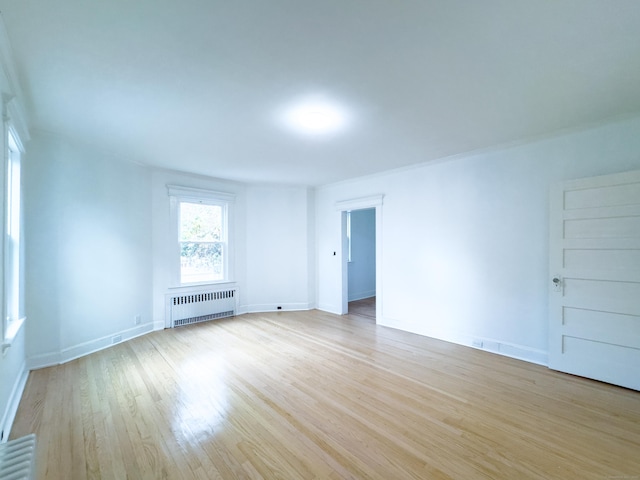 spare room with baseboards, radiator heating unit, and light wood-style floors