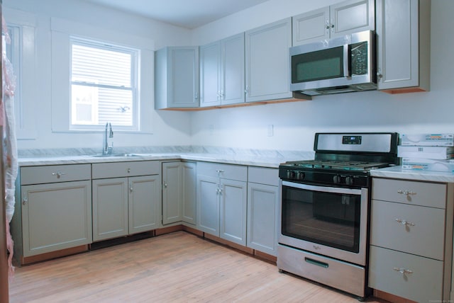 kitchen featuring light stone counters, stainless steel appliances, gray cabinets, a sink, and light wood-type flooring