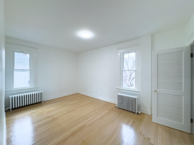 empty room featuring radiator, baseboards, and light wood-style floors
