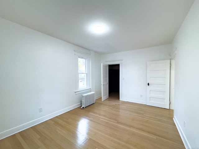 unfurnished bedroom with radiator heating unit, baseboards, and light wood-style flooring