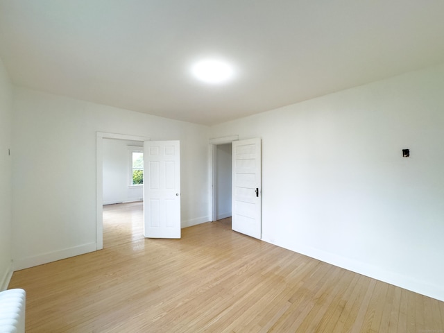 empty room with baseboards, radiator heating unit, and light wood-type flooring