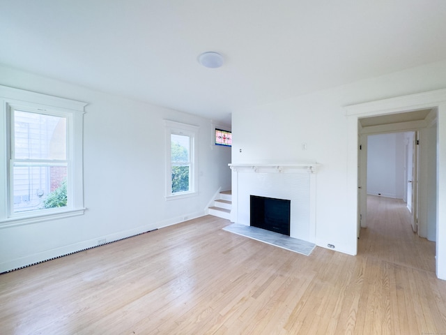 unfurnished living room featuring a fireplace with flush hearth, baseboards, and light wood-style floors