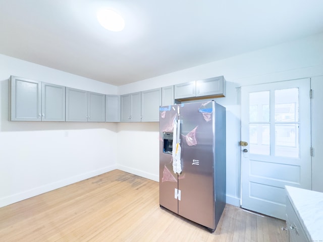 kitchen featuring light wood-style flooring, stainless steel fridge, baseboards, gray cabinetry, and light countertops