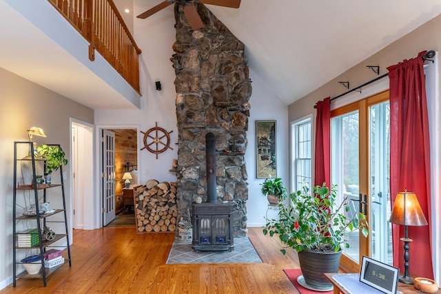living room with a wood stove, ceiling fan, baseboards, wood finished floors, and high vaulted ceiling