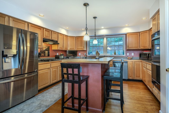kitchen featuring light wood-style flooring, appliances with stainless steel finishes, a center island, under cabinet range hood, and a kitchen bar