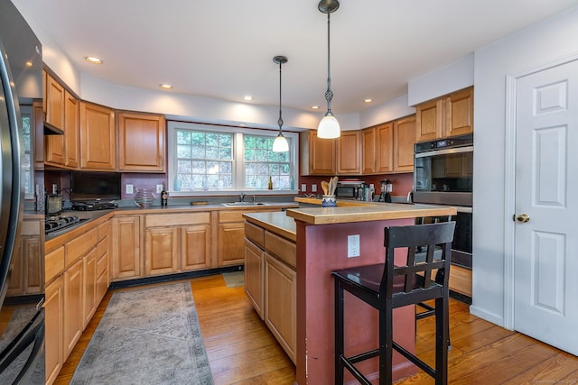 kitchen with a sink, a breakfast bar, light wood-style floors, a center island, and black appliances