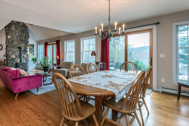 dining space with a wood stove, light wood finished floors, an inviting chandelier, and a wealth of natural light