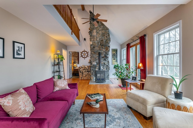 living area featuring a wealth of natural light, ceiling fan, high vaulted ceiling, and a wood stove