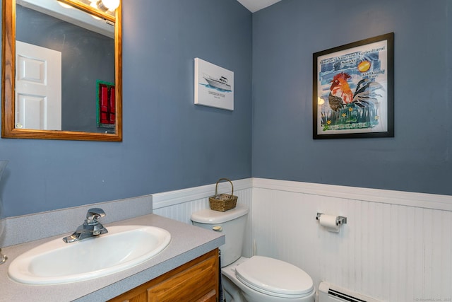 bathroom featuring baseboard heating, wainscoting, toilet, and vanity