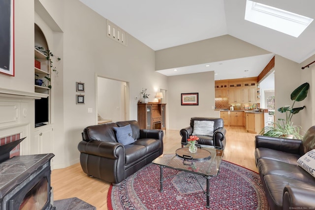 living room featuring a wood stove, light wood finished floors, a skylight, and built in shelves
