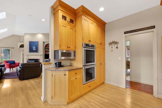 kitchen featuring light wood-style flooring, light brown cabinets, stainless steel appliances, open floor plan, and a fireplace