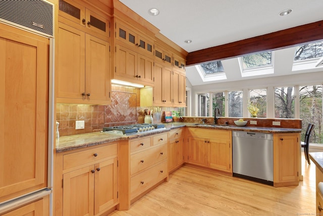 kitchen featuring tasteful backsplash, a skylight, appliances with stainless steel finishes, a sink, and a peninsula