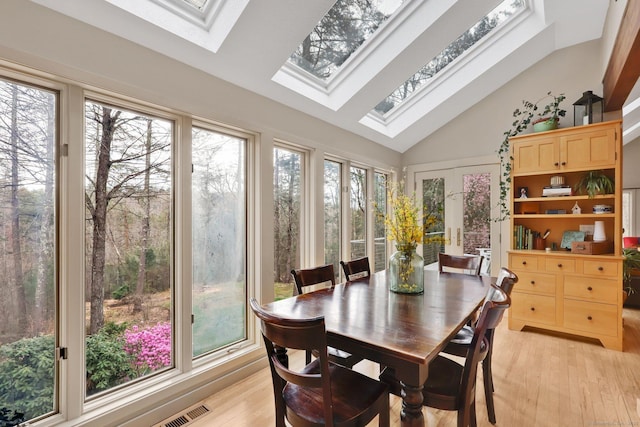 sunroom / solarium featuring wood finished floors, high vaulted ceiling, visible vents, and a skylight
