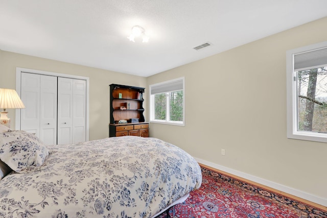 bedroom with a closet, visible vents, wood finished floors, and baseboards