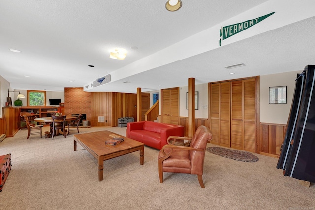 living area with stairway, wooden walls, a wainscoted wall, a textured ceiling, and light colored carpet
