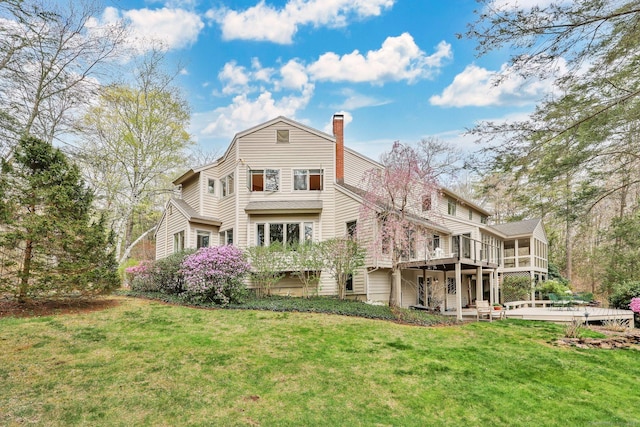 back of house featuring a chimney, a wooden deck, a sunroom, and a lawn