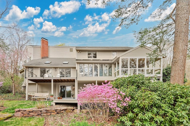 rear view of house featuring a chimney, a shingled roof, a deck, and a sunroom